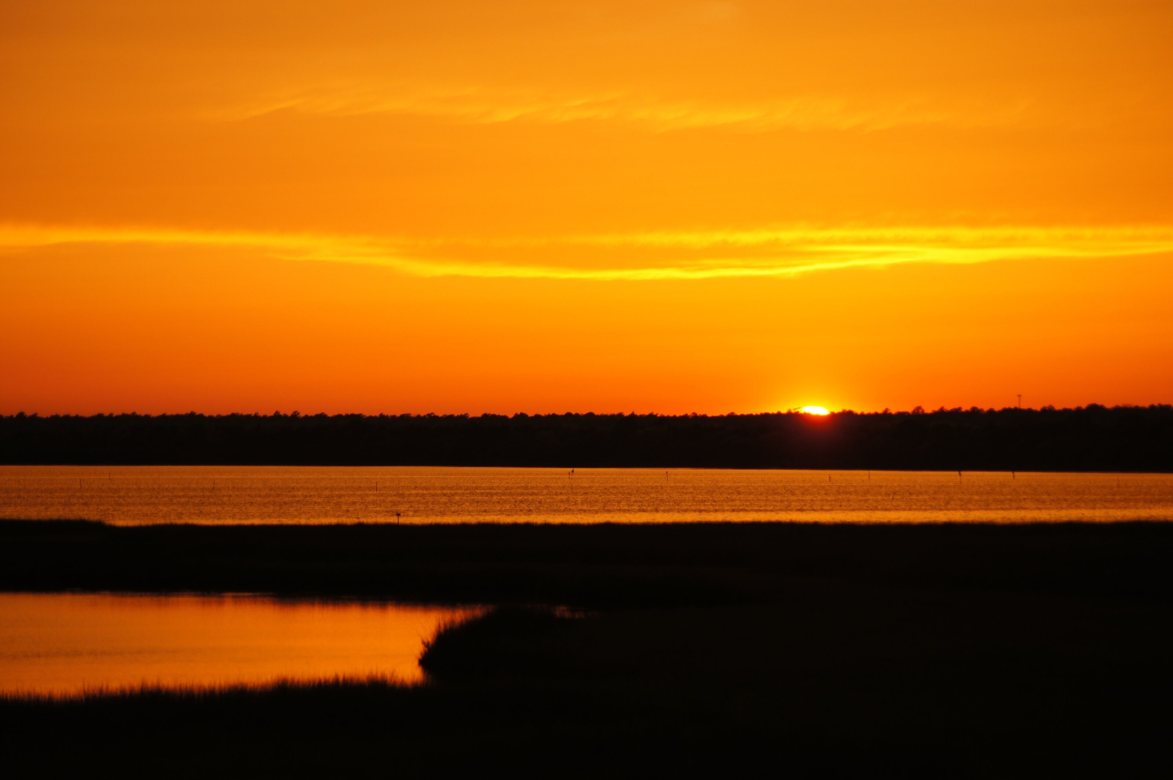 A sunset over a calm body of water with a distant shoreline.