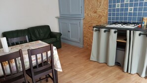 A dining area with a table set for two, a green sofa, and a kitchen with a gas stove. - Village center, Village house for 4 people (Florac)
