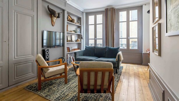 A living room with a sofa, armchairs, a TV, and a bookshelf.