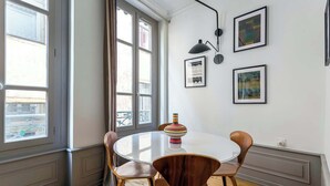 A dining area with a round table and four chairs, a vase with a striped pattern, and three framed artworks on the wall.