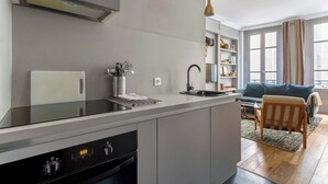 A modern kitchen with a built-in oven, a sink, and a dining area with a blue sofa and wooden chair.