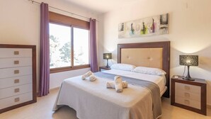 A hotel room with a bed, a nightstand with a lamp, a dresser, and a window with curtains.