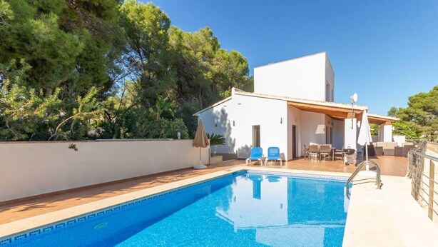 A swimming pool with a white building in the background, surrounded by trees.