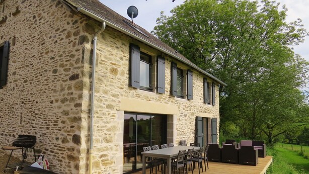 Ein Steinhaus mit Terrasse, Sitzgelegenheiten im Freien und einem großen Fenster.