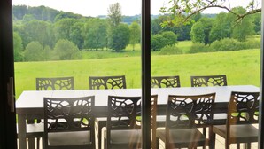 Ein Tisch und Stühle auf einer Terrrasse mit Blick auf ein grünes Feld und Bäume.
