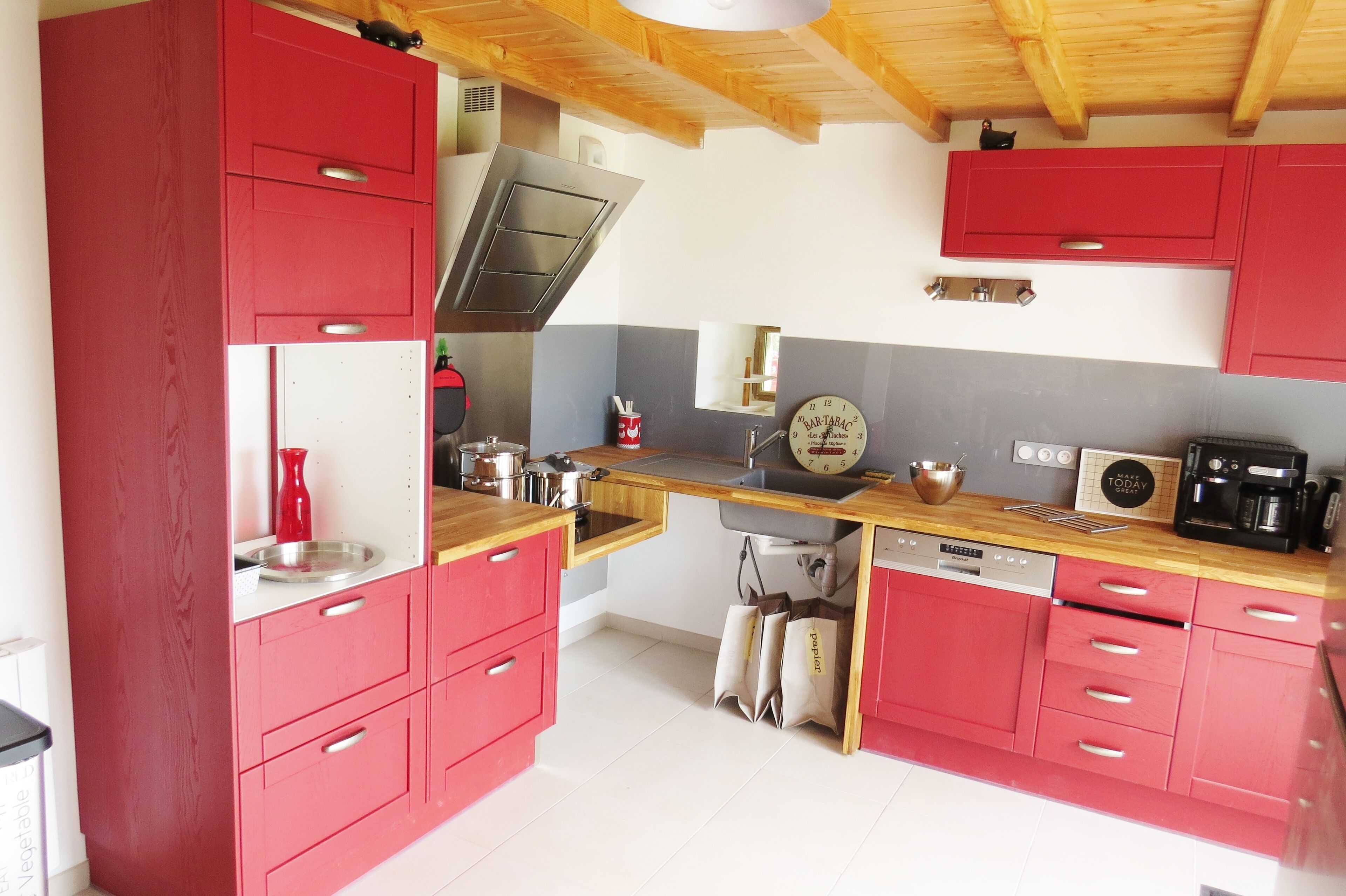 Una cocina con armarios rojos, techo de madera y una campana extractora de acero inoxidable.
