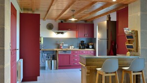 Eine Küche mit Holzbalken, einer roten Tür, rosa Schränken, einem Kühlschrank und Barhocker.