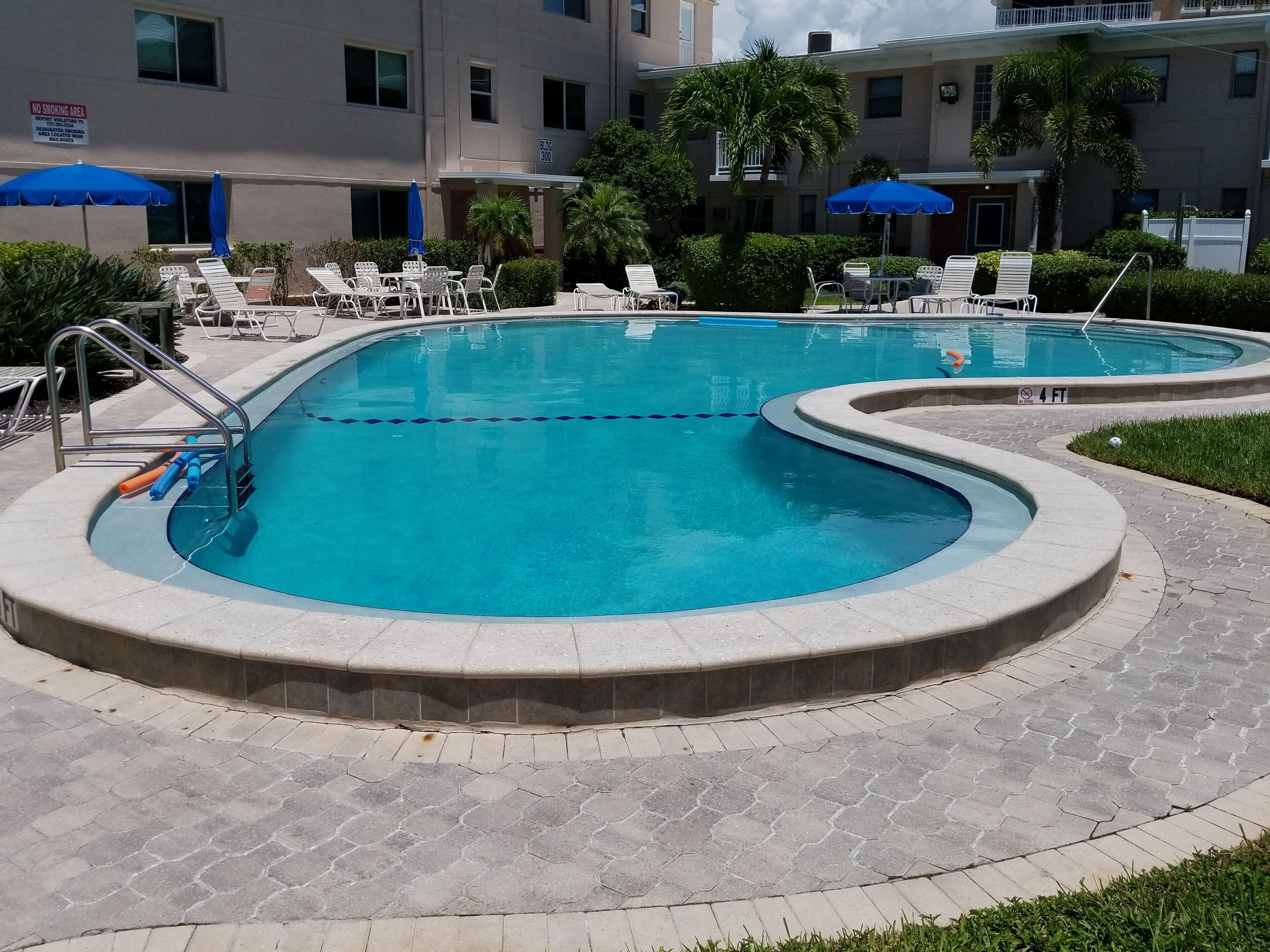 Une piscine avec une terrasse carrelée, des chaises longues et des parasols.