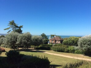 Une maison avec vue sur la mer, entourée d’arbres et dotée d’une pelouse bien entretenue.