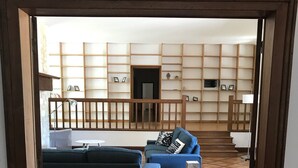Een woonkamer met een modulaire bank en een blauwe fauteuil, een houten boekenkast en een betegelde vloer.