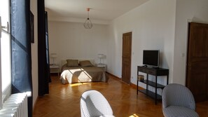 A bedroom with a bed, bedside lamps, a television on a stand, and a houndstooth patterned chair.