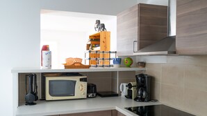 A modern kitchen with a microwave, toaster, coffee maker, and a wooden shelf with various items. - Gîte Écureuil: Lower Villa 2 Bedrooms, Terrace, Parking (Velaux)