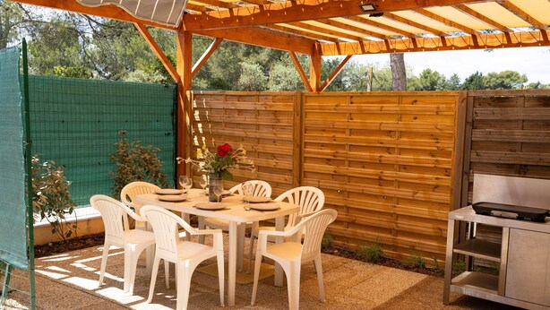 An outdoor patio with a wooden pergola, a table set for dining, white plastic chairs, and a grill station. - Gîte Écureuil: Lower Villa 2 Bedrooms, Terrace, Parking (Velaux)