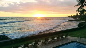 A poolside view with a sunset over the ocean, lounge chairs, and a clear sky.