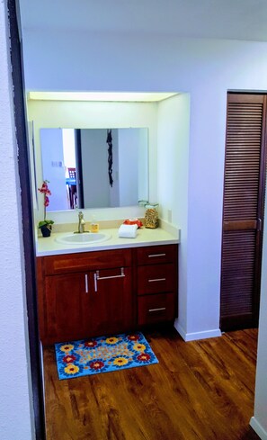 Une salle de bain avec un lavabo blanc, un meuble-lavabo en bois et un miroir au-dessus. Un tapis à motifs floraux bleus recouvre le sol.
