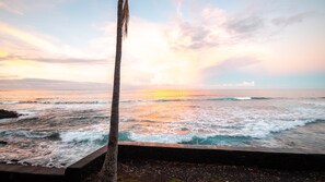 Une plage avec des vagues, un palmier et un coucher de soleil.