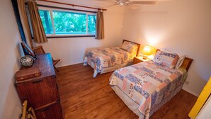 A bedroom with two beds, wooden flooring, a window with curtains, a bedside lamp, and a wooden dresser.