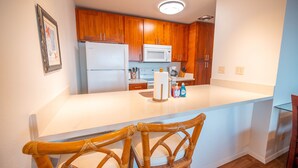 A kitchen with wooden cabinets, a white refrigerator, a microwave, and a wooden island with chairs.