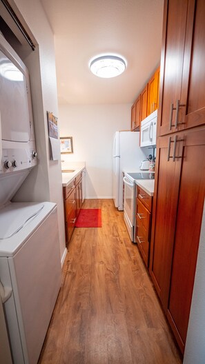 Une cuisine compacte avec des meubles en bois, un réfrigérateur blanc, un four à micro-ondes et un lave-linge.