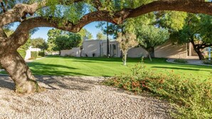 Un jardin bien entretenu, avec une pelouse, des allées de gravier et des arbres adultes.