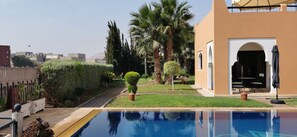 A swimming pool with a clear view of the surrounding garden and a building with an arched entrance. - Beautiful Riad Asmaa near Agadir (10kms).  Large private pool. 5 bedrooms (Ibn Ayaden)