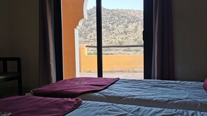 Camera d'albergo con un letto, una sedia e vista su un paesaggio collinare attraverso una finestra.