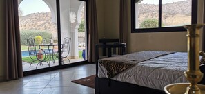 A bedroom with a bed, a nightstand, a lamp, and a view of a patio with a table and chairs. - Beautiful Riad Asmaa near Agadir (10kms).  Large private pool. 5 bedrooms (Ibn Ayaden)