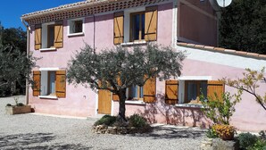 Una casa de dos pisos con fachada rosa, contraventanas de madera y camino de entrada de grava.