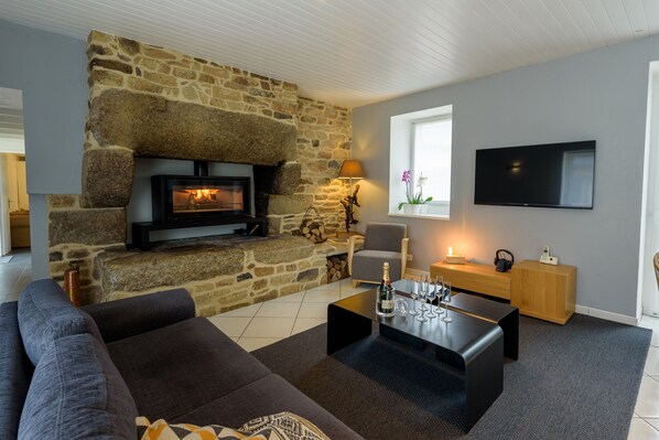 A modern living room with a stone fireplace, a flat-screen TV, a sofa, and a coffee table with a bottle and glasses.