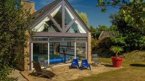 Een modern huis met een glazen orangerie, een zwembad en terrasmeubels.