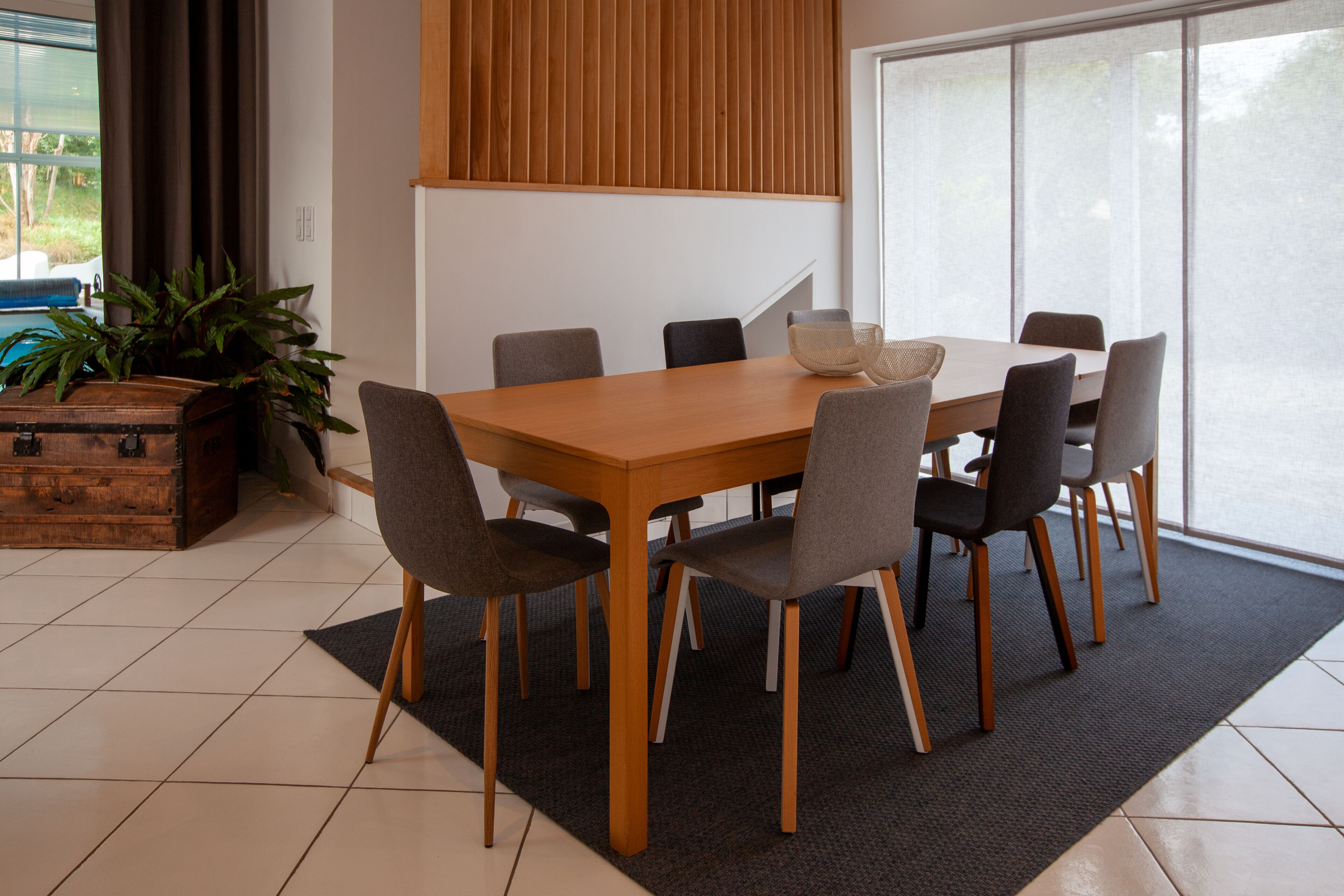 Een eetgedeelte met een houten tafel en stoelen, een potplant en een groot raam met uitzicht.