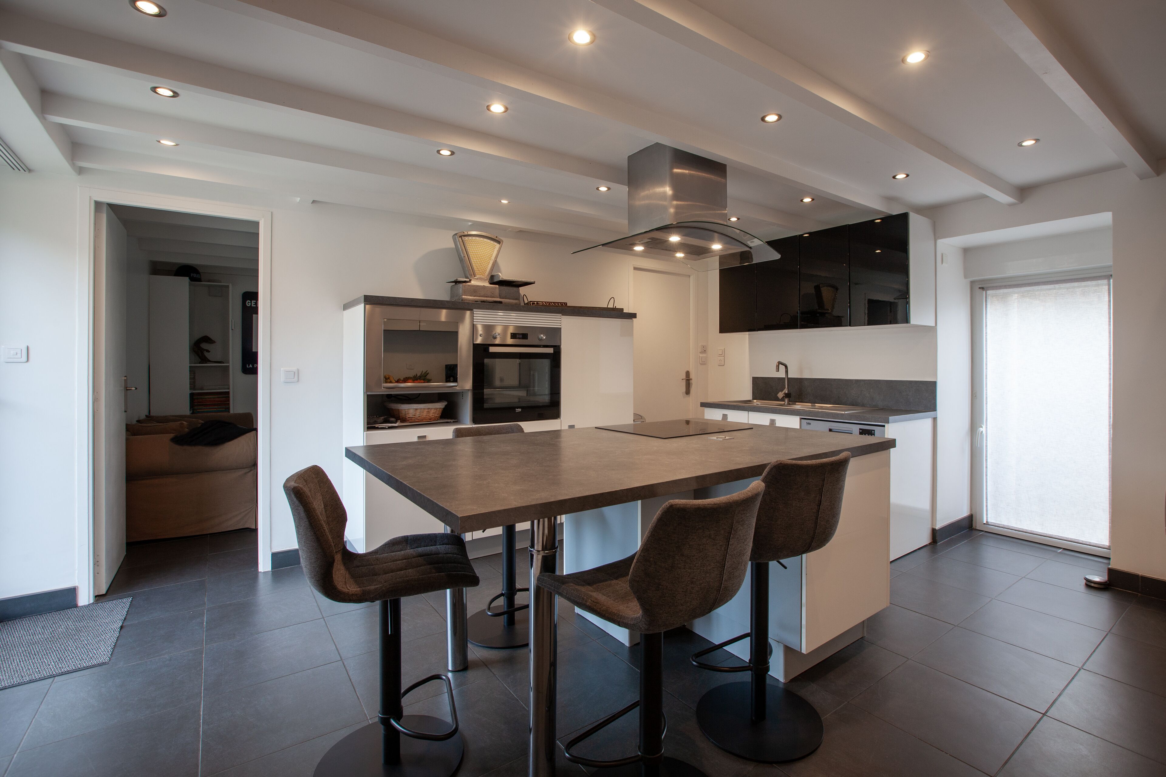 A modern kitchen with a central island, bar stools, a built-in oven, and a stainless steel range hood.