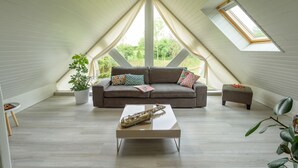 Een moderne loft slaapkamer met een schuine plafond, een groot raam, een bank, een bijzettafeltje en een potplant.