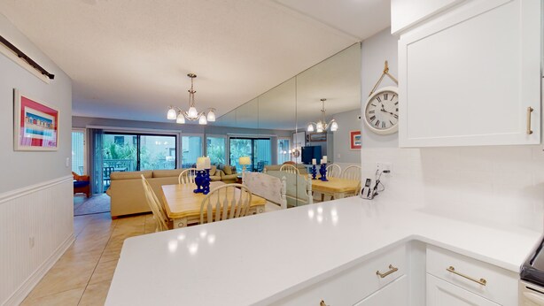 Una cocina moderna con armarios blancos, una isla grande y una zona de comedor con mesa y sillas de madera.