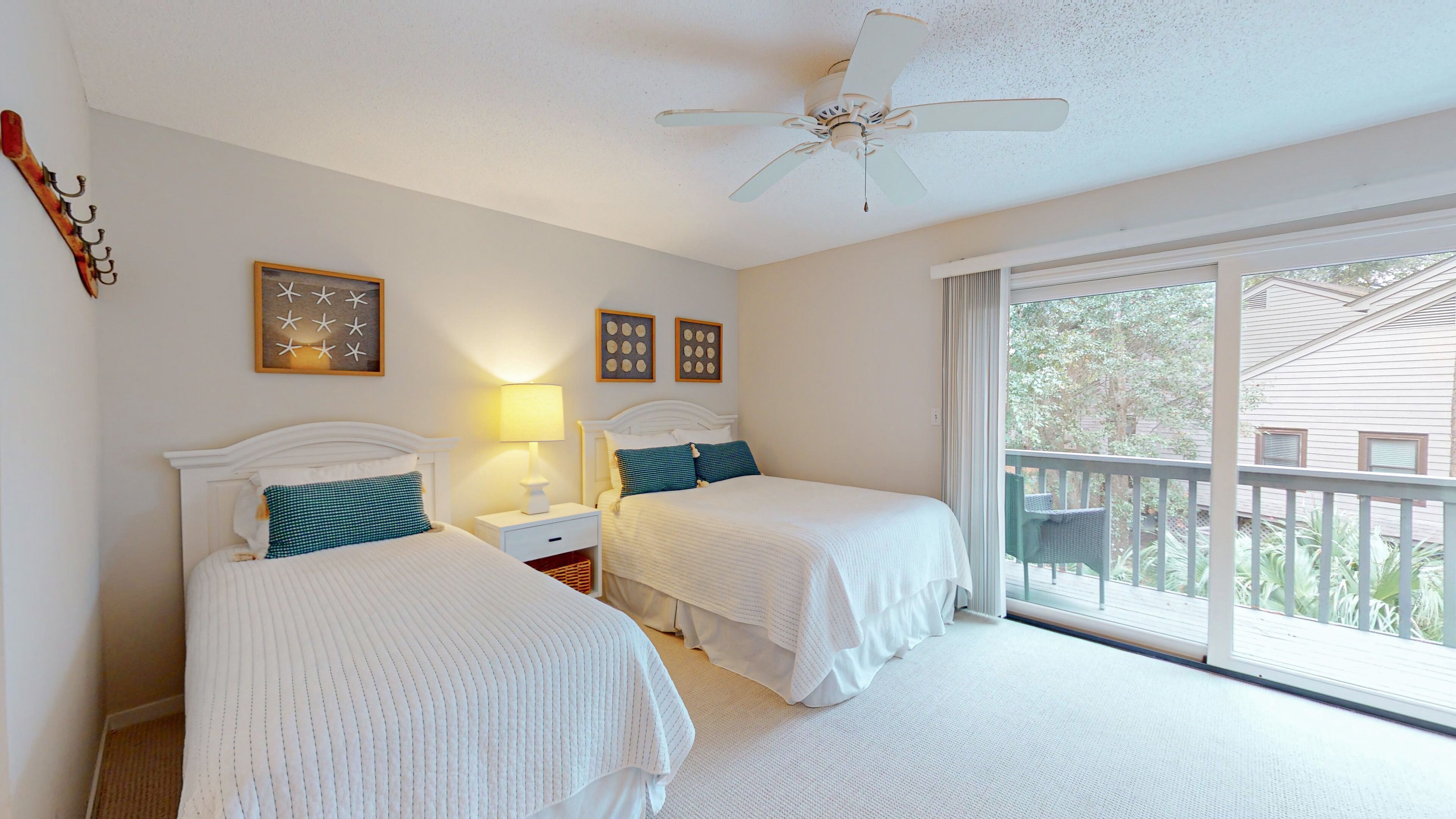 A bedroom with two beds, a ceiling fan, and a large window with a view of the outside.