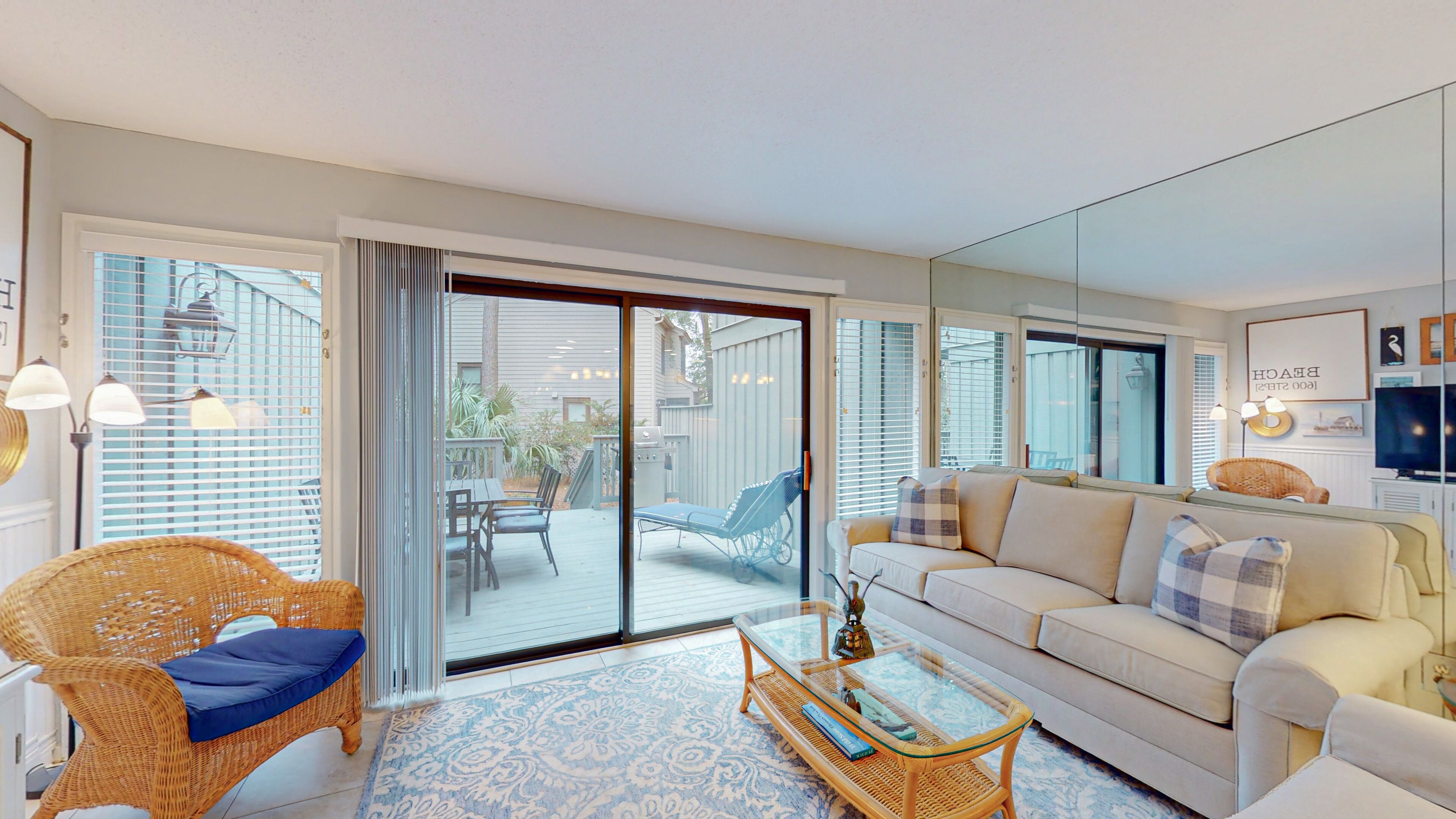A spacious living room with a large sliding glass door leading to an outdoor patio, a comfortable sofa set, a wicker chair, and a glass coffee table.