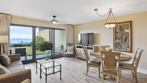 Een ruime woonkamer met een grote schuifpui naar een balkon, een flatscreen televisie en een eethoek met houten stoelen en een tafel.