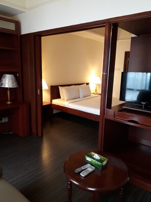 A hotel room with a bed, bedside lamps, a TV, a table with remote controls, and a wardrobe.