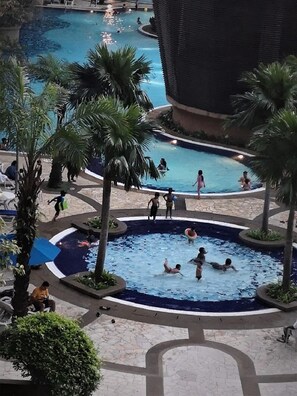 A pool area with multiple swimming pools, palm trees, and people swimming and relaxing.