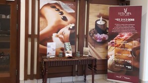 A reception area with a wooden reception desk, a large poster advertising spa services, and a sign detailing the spa's operating hours and services. - Cool Service Suites at Times Square (Kuala Lumpur)