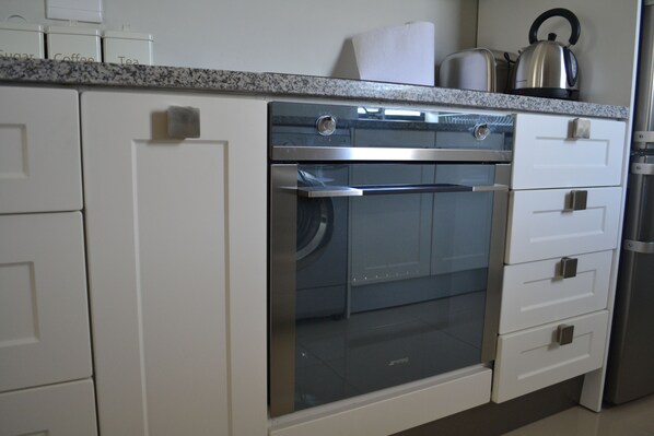 Una cocina con horno integrado, muebles blancos y encimera de granito.