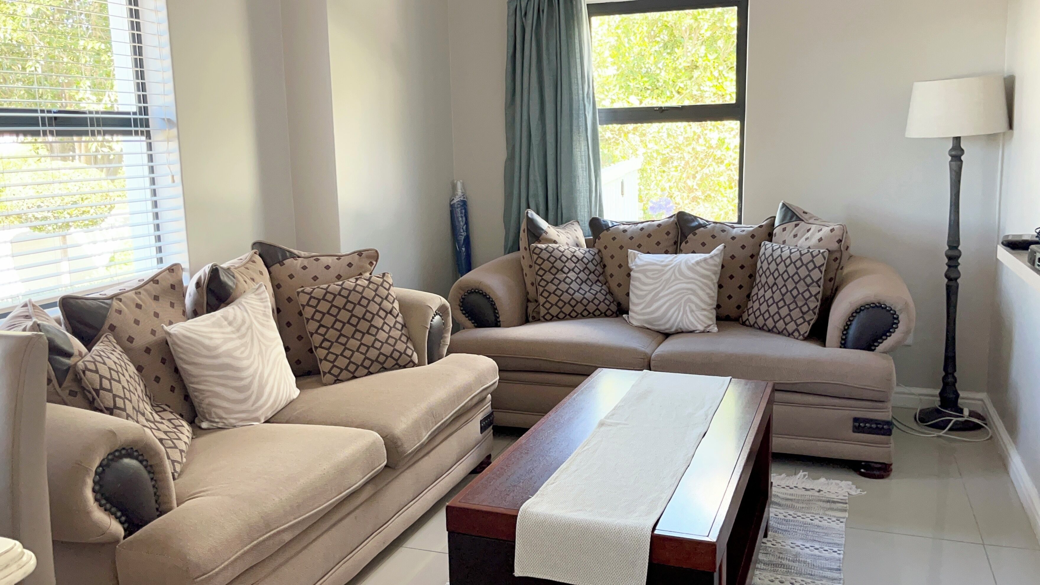 A living room with a beige sofa set, patterned cushions, a wooden coffee table, and a floor lamp.