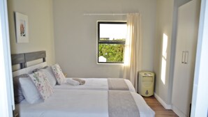 A double bed with floral pillows, a window with a view of greenery, and a bedside heater. - Cape Town Luxury  Self Catering Home in a Working Wine Farm - Family Friendly (Cape Town)