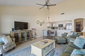 A spacious living room with a television, a dining area, and a kitchen in the background.
