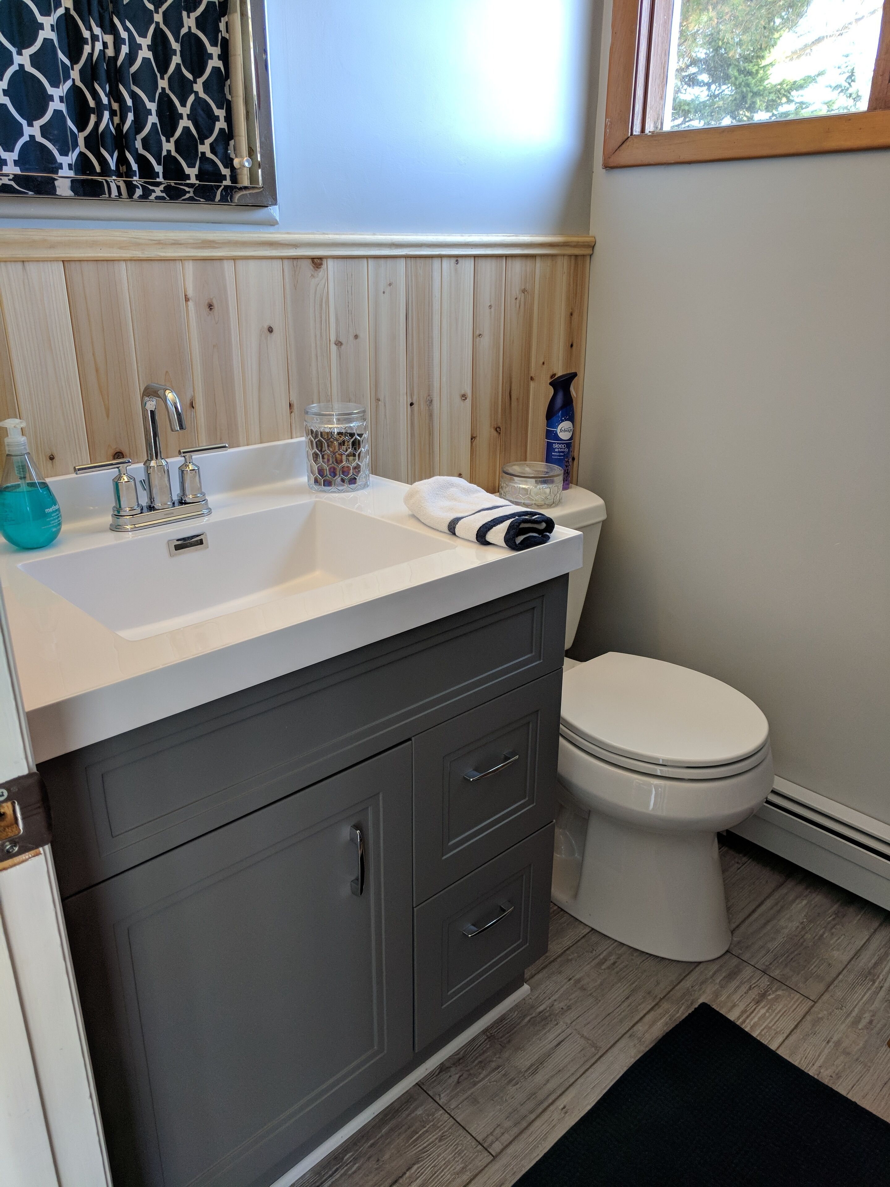 Ein Badezimmer mit einem weißen Waschbecken, einem dunkelgrauen Schrank und einer weißen Toilette.