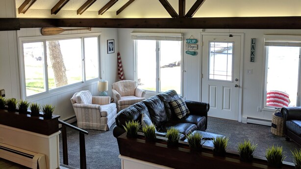 A spacious living area with a high ceiling, exposed wooden beams, a leather sofa, and a view of the outdoors through large windows. - Hamptons style Lake house on Sunset point. With water on both the east and west! (Lindstrom)