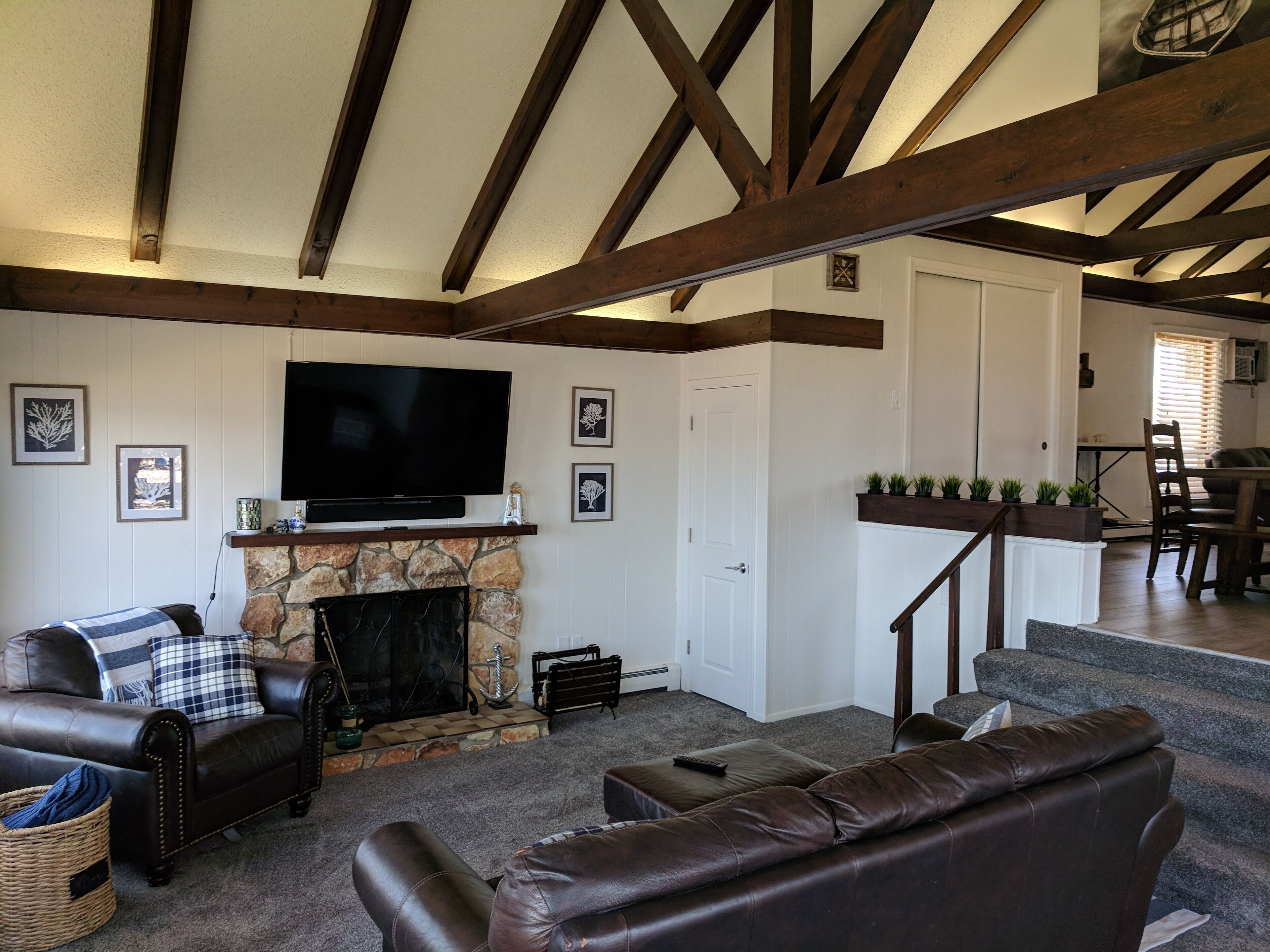 A living room with a stone fireplace, leather sofas, a flat-screen TV, and a staircase leading to another room.