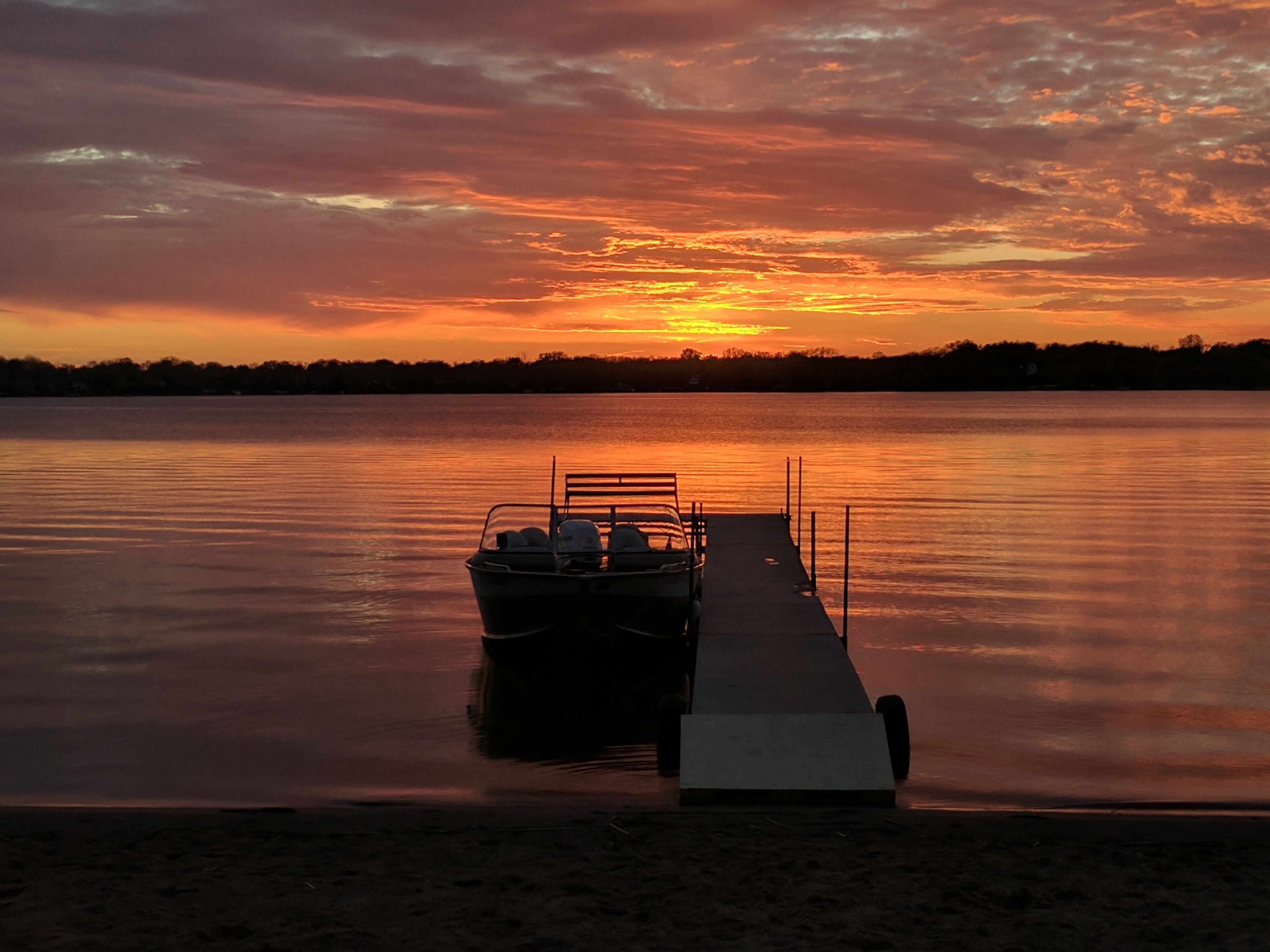 Un bateau était amarré à un quai qui s’étendait sur une étendue d’eau calme, au moment du coucher du soleil.