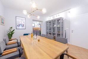 Zona pranzo moderna con tavolo in legno, sedie rivestite in grigio, un lampadario e un mobile con ante in vetro.