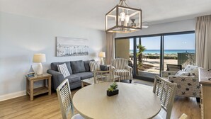 Una sala moderna con una mesa redonda, dos sofás y un comedor. Hay un ventanal con vistas a la playa.